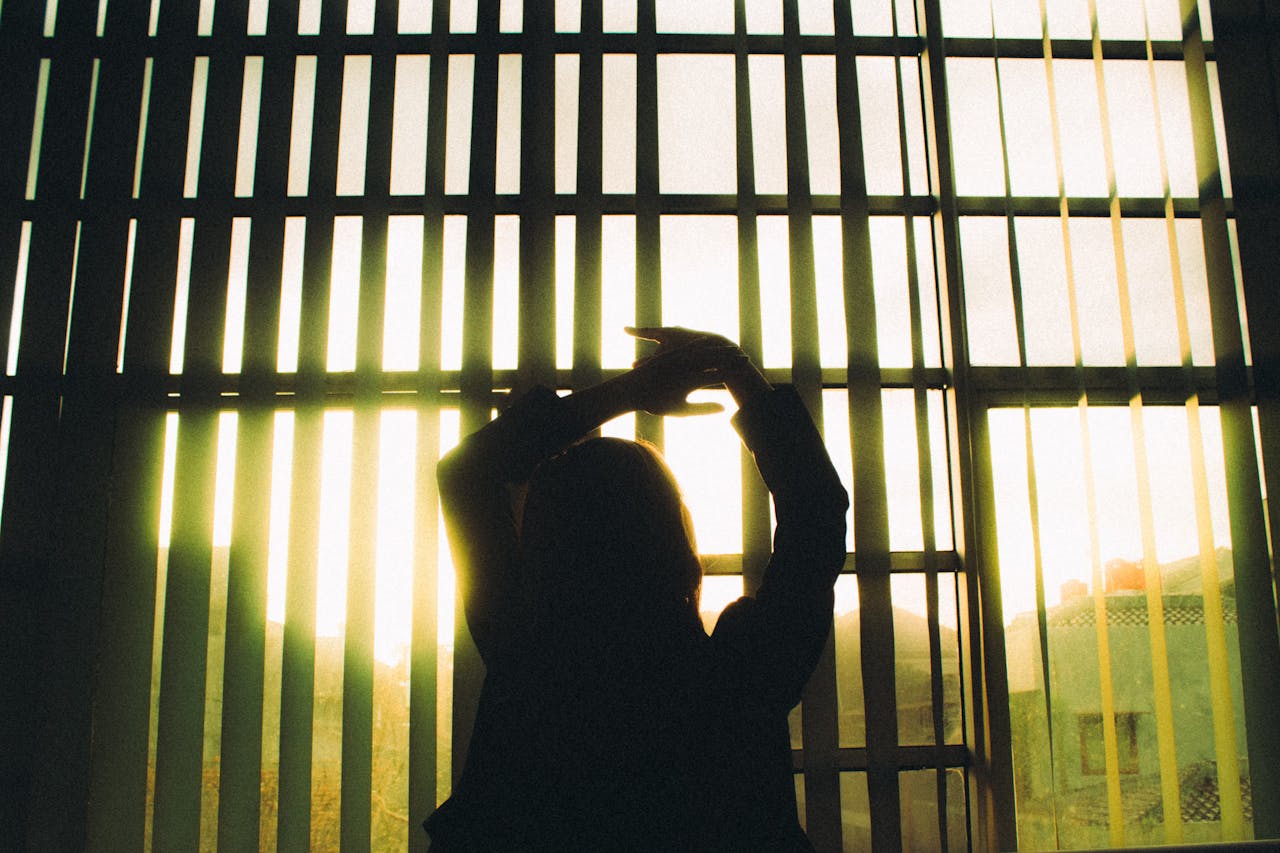 about-06 Silhouette of a woman stretching in front of large window blinds with sunlight streaming in.