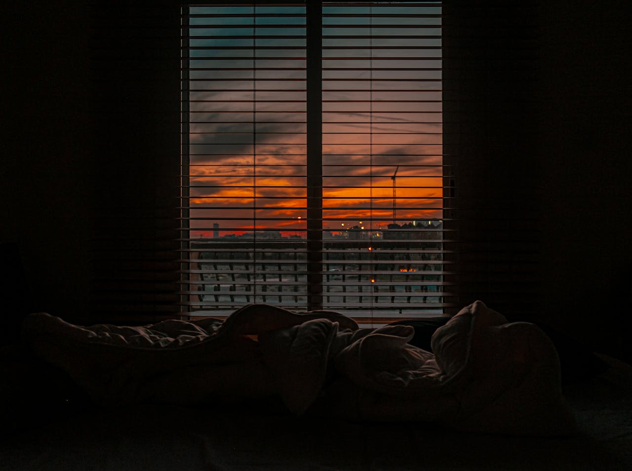 why-choose-us-02 Cozy bedroom with a view of a vibrant sunset through window blinds.